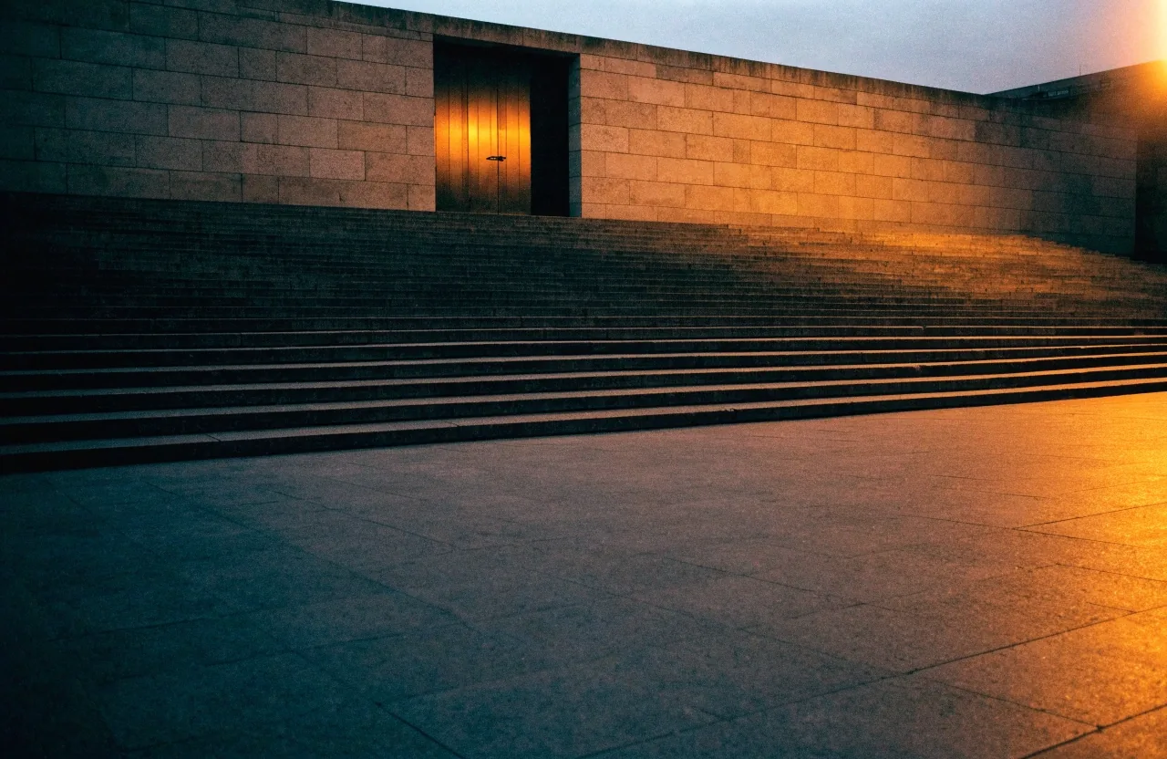 Escalinata y puerta institucional vacías al anochecer, vistas desde el otro lado de la plaza