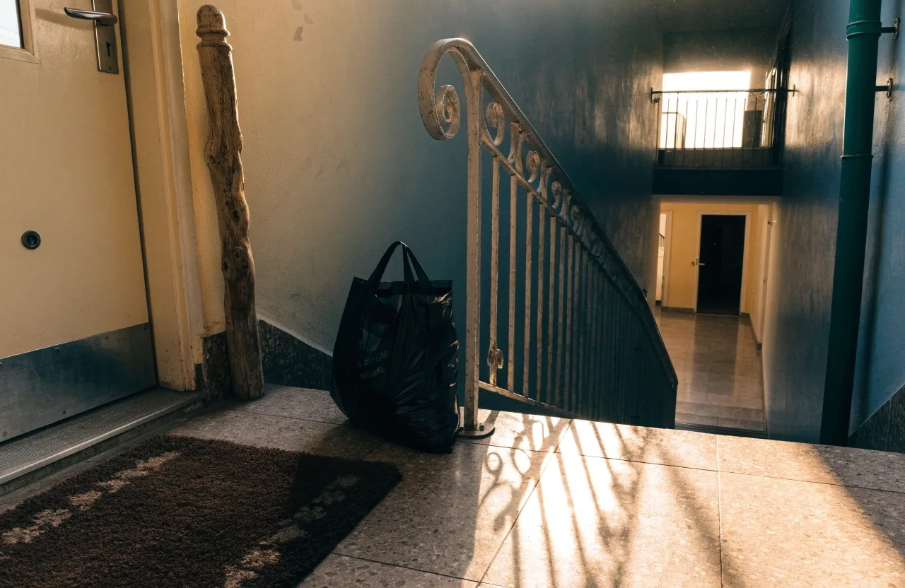 Calle residencial al atardecer con una puerta de entrada, una bicicleta apoyada y luz cálida en una ventana