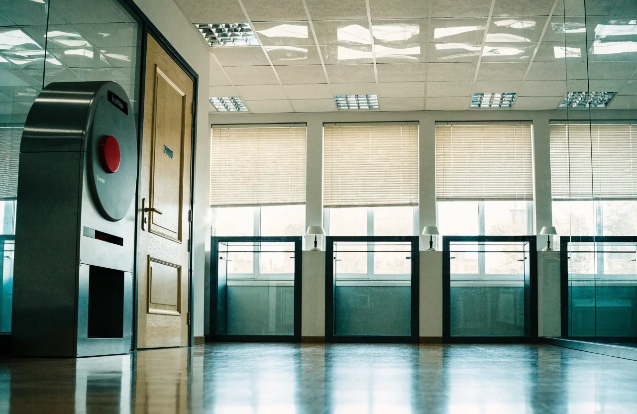 Sala vacía de atención al público con dispensador de turnos y ventanillas tras cristales