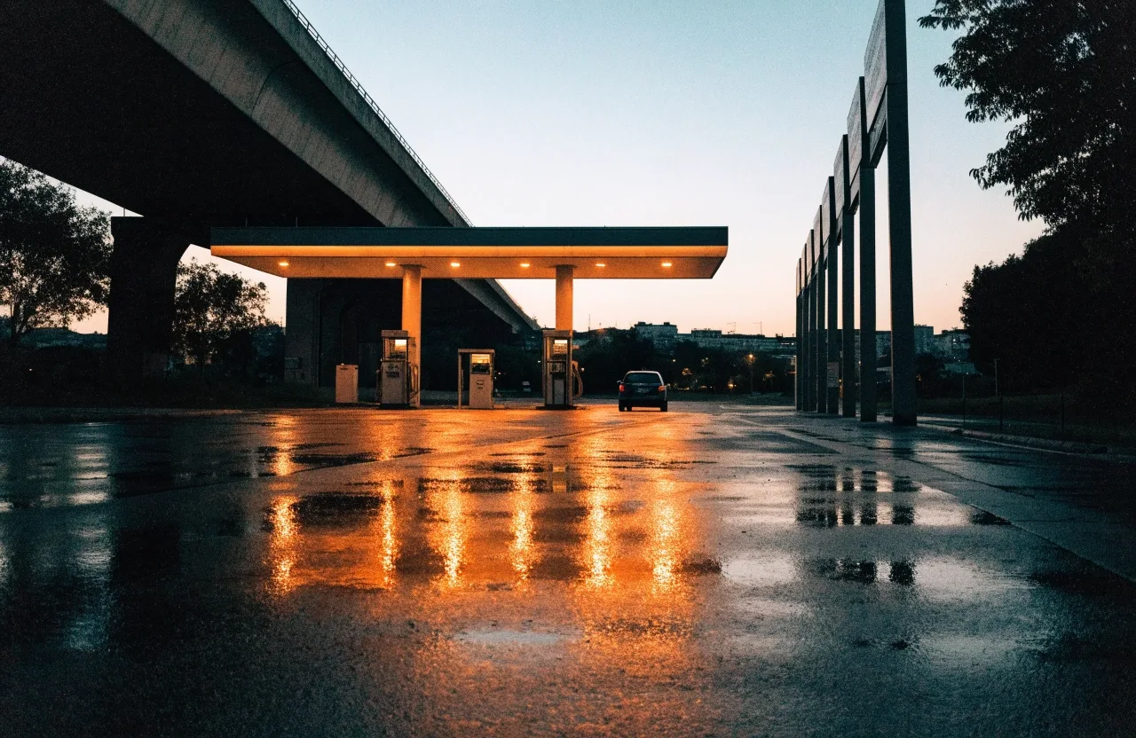 Estación de servicio nocturna con luz ámbar sobre el pavimento mojado