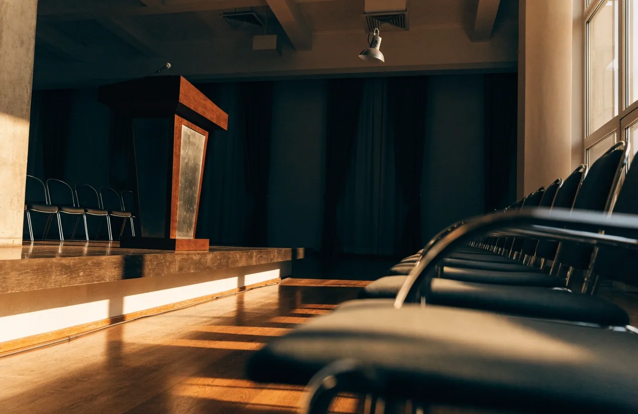 Sala de prensa institucional vacía al atardecer, con atril y sillas desocupadas