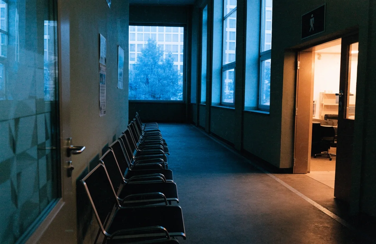 Pasillo institucional al atardecer con sillas vacías junto a una sala de reuniones cerrada
