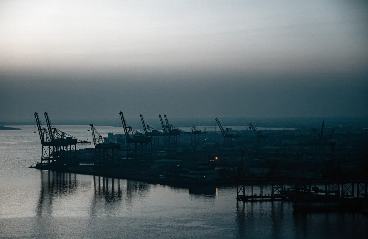 Perfil portuario asiático al amanecer visto desde lejos, con grúas de carga y torres en silueta